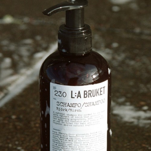Eine dunkelbraune Shampoo-Flasche mit Pumpe steht auf schlammigem Boden.