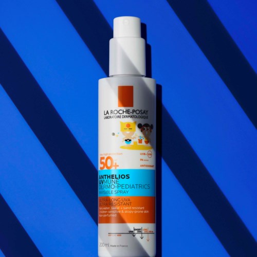 A white sunscreen bottle with an orange and blue label, placed on a blue background with dark blue stripes.