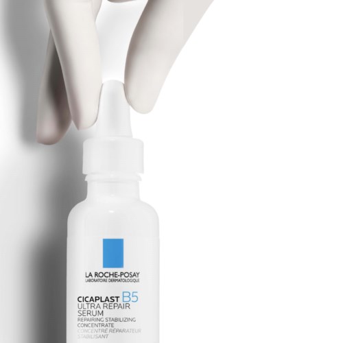 Een klein witte fles met La Roche-Posay-logo, vastgehouden door een hand met handschoenen.