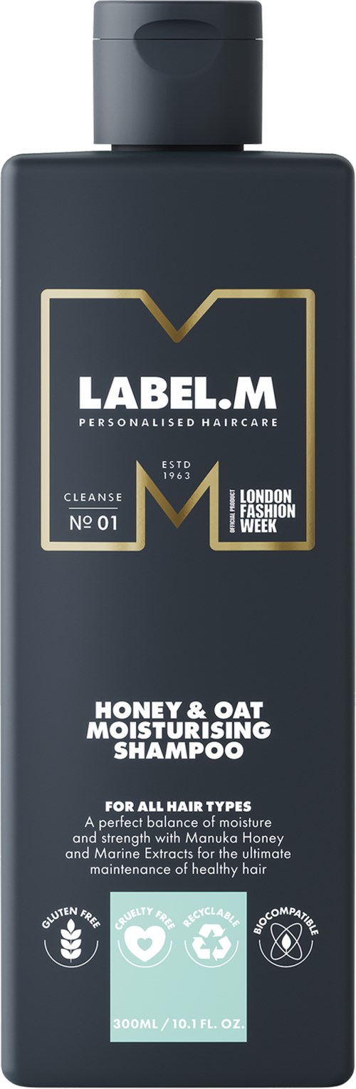 En mörkgrå flaska hårvårdsprodukt med guld- och vit text och ikoner, märkta Honey & Oat Moisturising Shampoo.