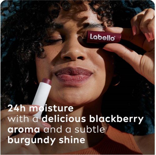 Een vrouw brengt lippenstift aan, promoot een product met vocht, bessenaroma en burgundy glans.