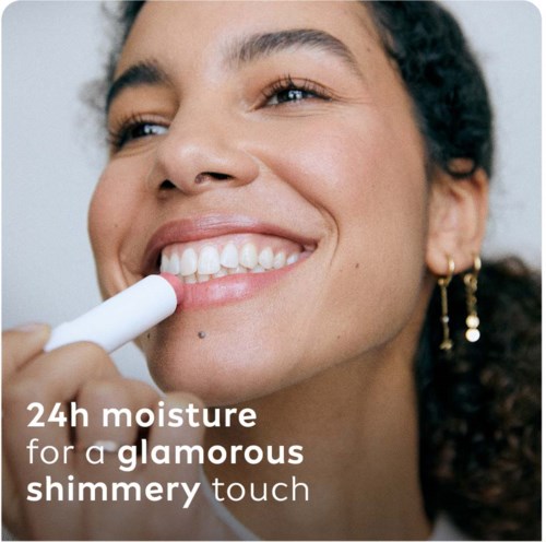 Een vrouw brengt lipstick aan en glimlacht, promoot 24 uur hydratatie voor een glanzende uitstraling.