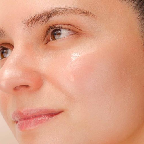 Close-up van het gezicht van een vrouw met heldere huid, bruine ogen en een zachte glimlach.
