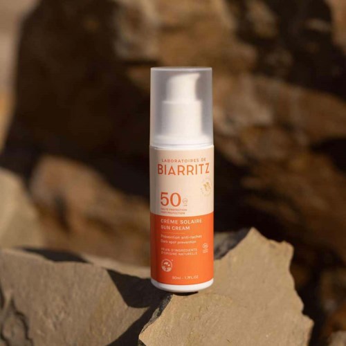 Zonnebrandcrèmefles met SPF 50 op een rots, buiten met een wazige natuurlijke achtergrond.