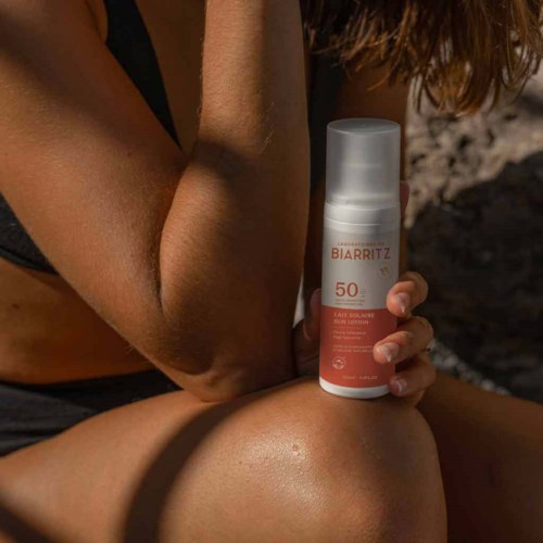 Iemand houdt een flesje Biarritz SPF 50 zonnebrandcrème buiten in de zon.