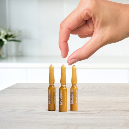 A hand is placing a small orange vial between three similar vials on a table. The vials are labeled.