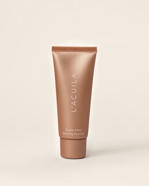 En metallisk bronsrör märkt 'L'ACULA Golden Hour Bronzing Face Gel' mot en enkel bakgrund.