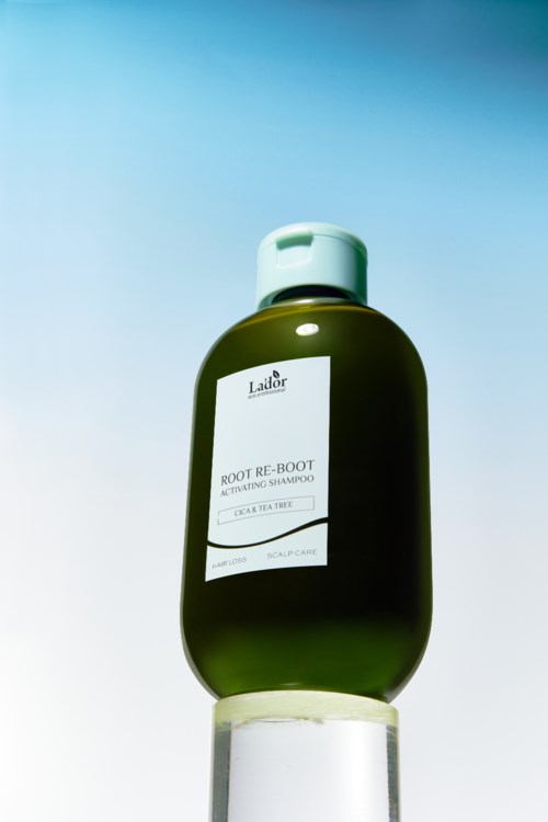 Een groene fles La'dor Root Re-Boot shampoo met een witte dop, geplaatst op een witte ondergrond tegen een lichtblauwe achtergrond.