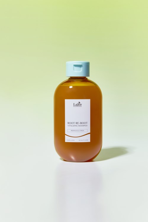 Een bruine shampoofles met een witte dop. Het label zegt 'Root Re-Boot'. Het staat op een lichte achtergrond.