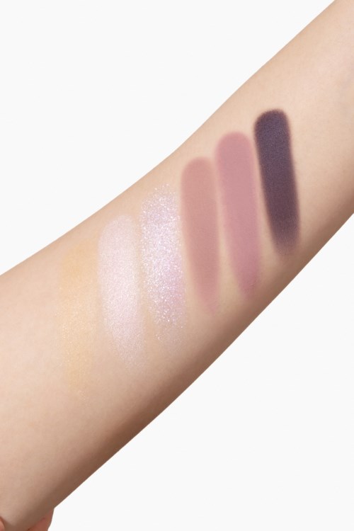 Swatches van verschillende oogschaduwkleuren op iemands arm, inclusief lichte, roze en donkere tinten.