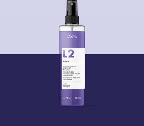 Een fles Lakme L2 Blonde Instant Detangling Conditioner met spraydop. Paarse en witte label. Tweedelige achtergrond.