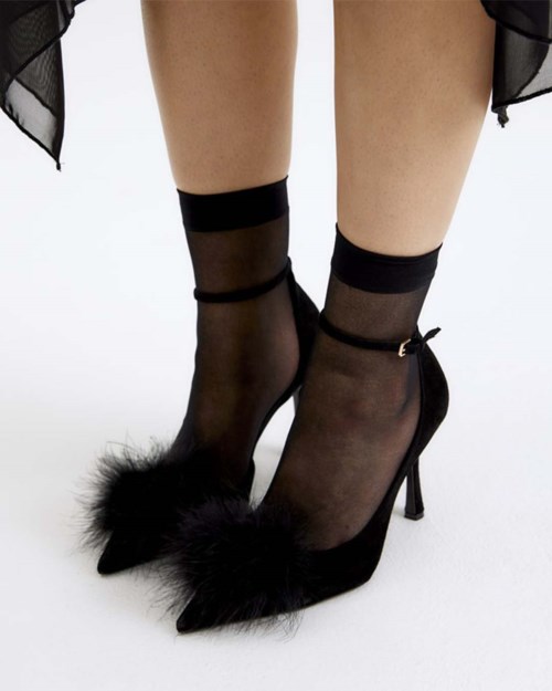 Schwarze High Heels mit Fellspitzen getragen mit transparenten schwarzen Socken. Die Schuhe sind stilvoll und elegant.