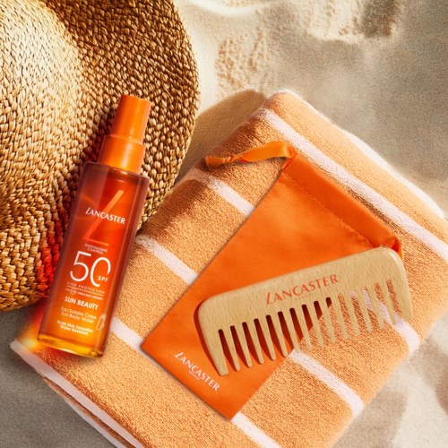 Een zonnebrand spray, oranje portefeuille, kam en beige handdoek liggen op het zand.