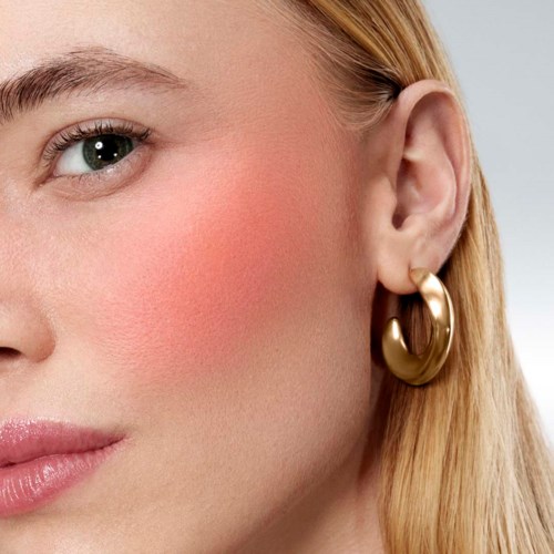 Close-up of a woman's face showing her eye, cheek with blush, and a gold earring.