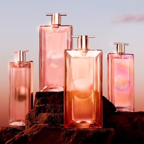 Fyra rosa parfyllådor av olika storlekar står på stenar, med en rosa och lila himmel i bakgrunden.