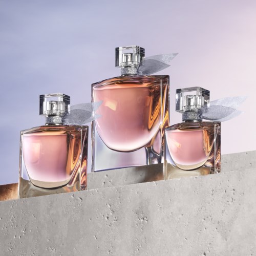 Drie parfumflesjes met roze vloeistof en zilveren doppen staan op een betonnen oppervlak. Ze hebben kleine decoratieve vleugels.