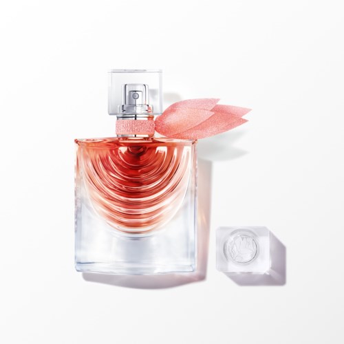 En transparent parfymflaska med rosa vätska och en rosa tygblomma på locket, placerad på en vit bakgrund.
