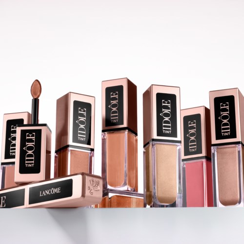 Mehrere Flaschen Lippenstift oder Lipgloss in Pink- und Beigeschattierungen sind auf einer weißen Oberfläche angeordnet.