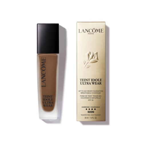 A beige foundation bottle with a black cap beside a cream-colored box with black text and a rose illustration.