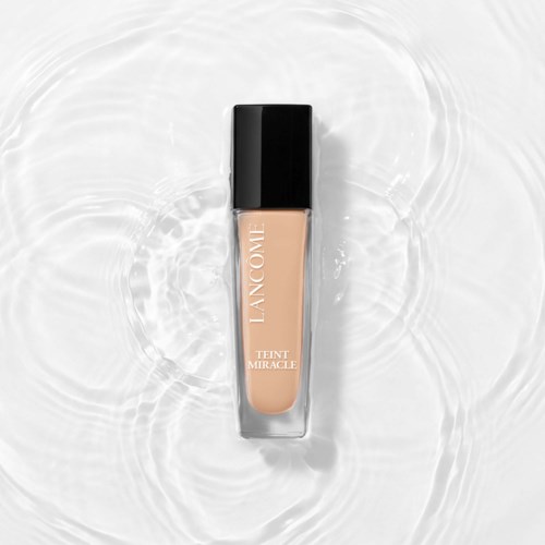 Een fles Lancôme Teint Miracle foundation die in water drijft met ringen eromheen.