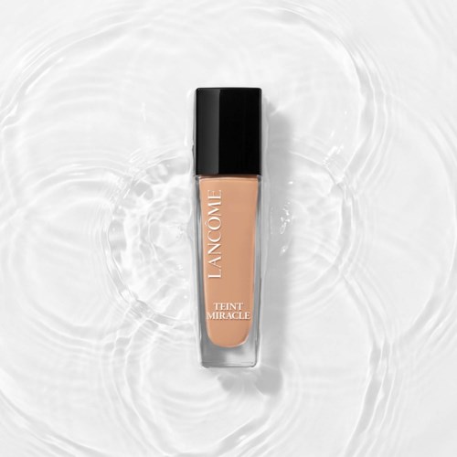 A beige liquid foundation in a clear bottle with black cap, placed in water with ripples.
