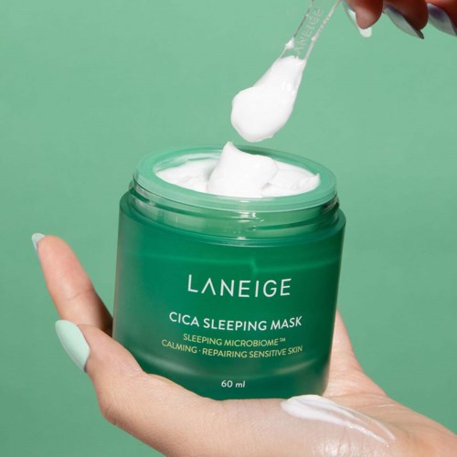 Een hand houdt een groene pot Laneige Cica Sleeping Mask. Een spatel haalt witte crème uit de pot.