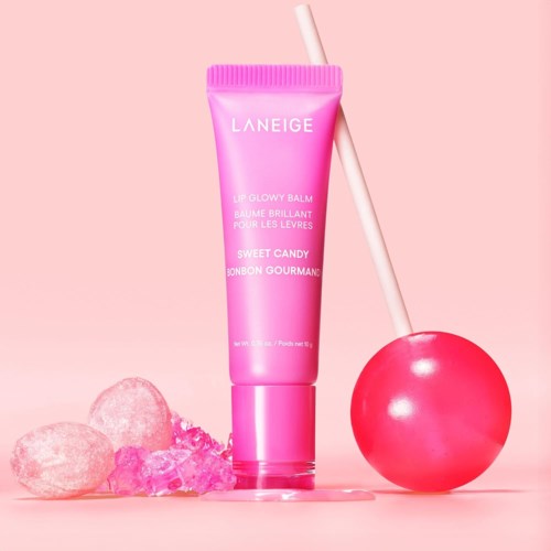 Een roze tube van Laneige Lip Glowy Balm met snoepjes en een roze lolly ernaast.
