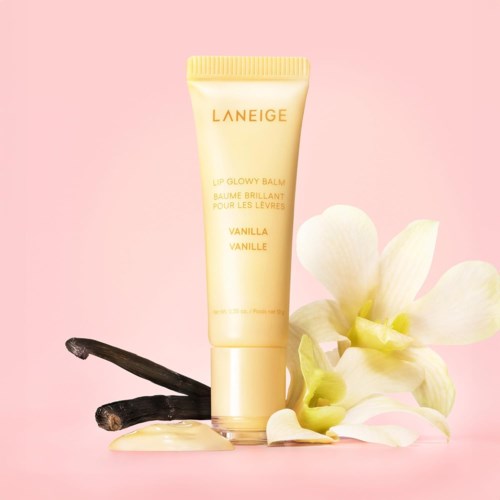 Lipbalsem tube met vanillesmaak, omgeven door vanilestokjes en witte bloemen op een roze achtergrond.