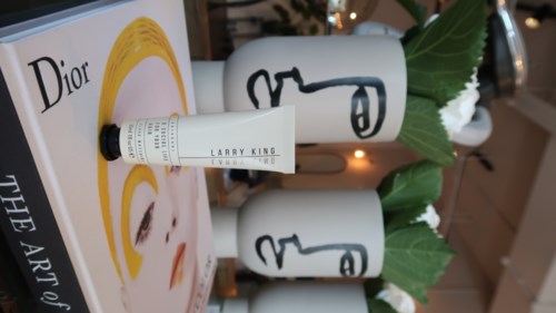 Ein Hautpflegeprodukt vor einem Dior-Magazin, mit drei nebeligen weißen Vasen mit Gesichtsskizzen, grünen Blättern und kleinen Lichtern.