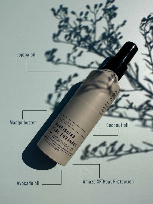 Flasche mit Haaröl, Schatten eines Baumzweigs auf Hintergrund. Etiketten erwähnen Jojoba-, Mango-, Kokos- und Avocadoöl.