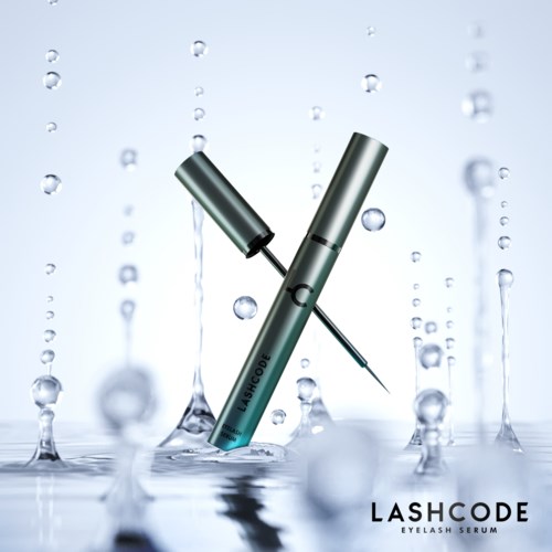 Een zilveren oogserumfles met een zwarte applicator, omgeven door waterdruppels. De merknaam 'LASHCODE' onderaan.