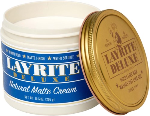 A white container with blue label and gold lid, holding natural matte cream for skin. The lid has a logo and text.