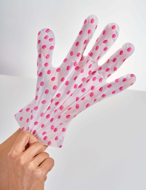 En hand håller en vit handskar med rosa prickar, verkar vara en städ- eller trädgårdshandske.