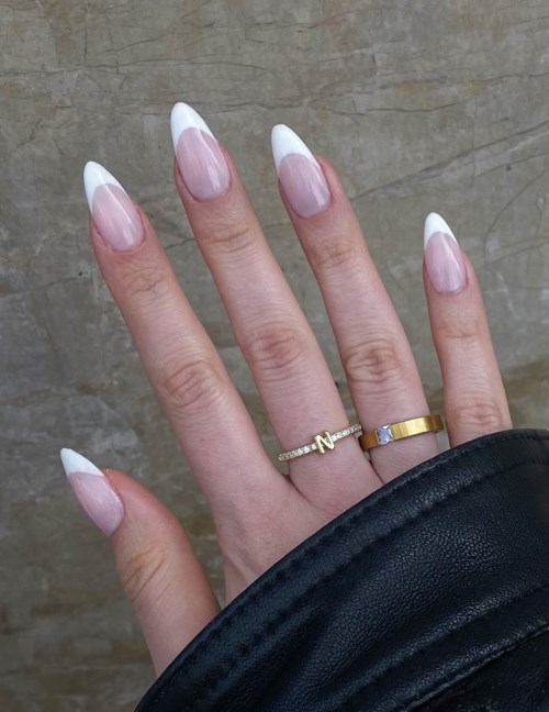 Hand with long nails, rings, and a black sleeve, against a gray textured background.