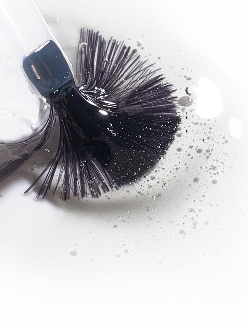 A black hairbrush with flexible bristles tangled in water and soap bubbles. It appears to be cleaning or washing.