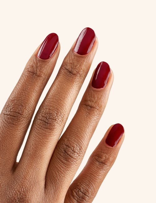 A hand with four fingers showing, nails painted in dark red color, on a light background.