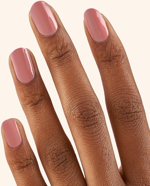 Four fingers with pink, well-manicured nails and smooth skin. The background is plain and light-colored.