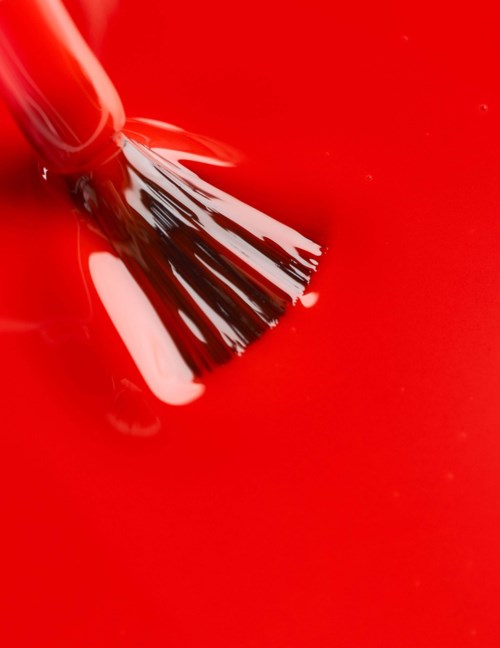 A nail polish brush is applying dark red polish on a surface.