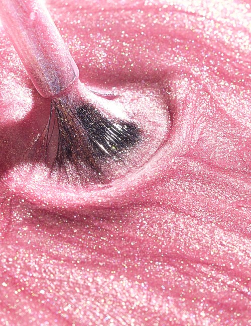 A makeup brush is applying pink, glittery face product with shimmer on a person's skin.