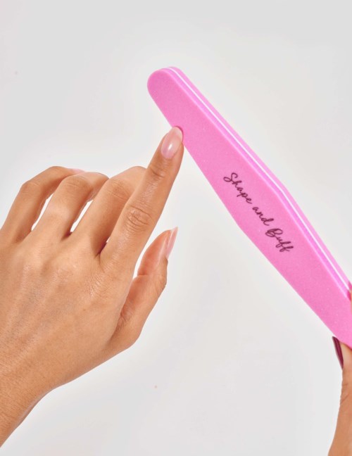 A hand reaches out to a pink nail file with the words "Smile and be kind" written on it.
