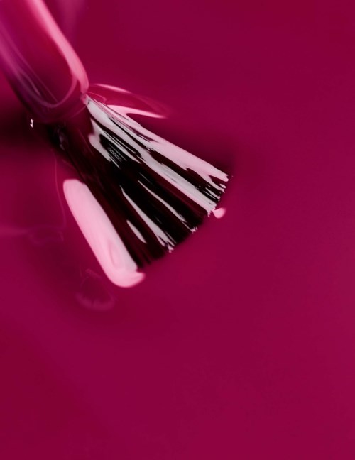 A makeup brush with pink nail polish on a deep pink background.