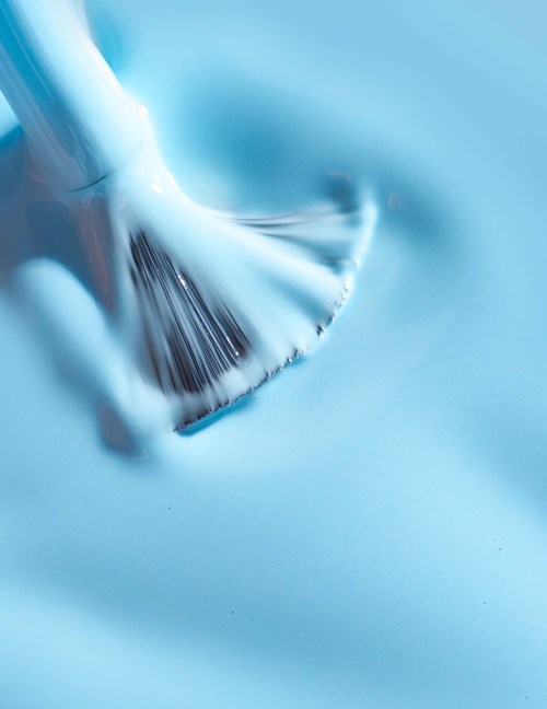 A paintbrush is spreading blue paint smoothly on a surface.