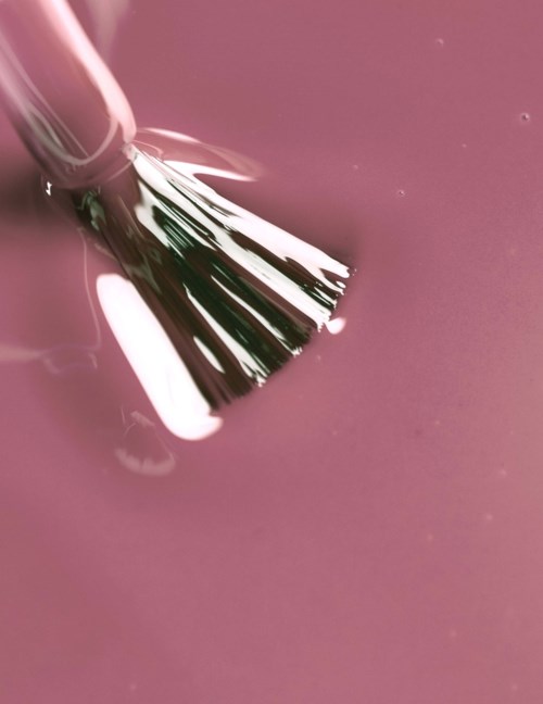 A brush spreads white paint on a pink surface in a close-up shot.