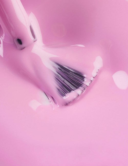 En rosa tandborste borstar vitt skum i rosa vätska. Scenen är mjuk och ljus.