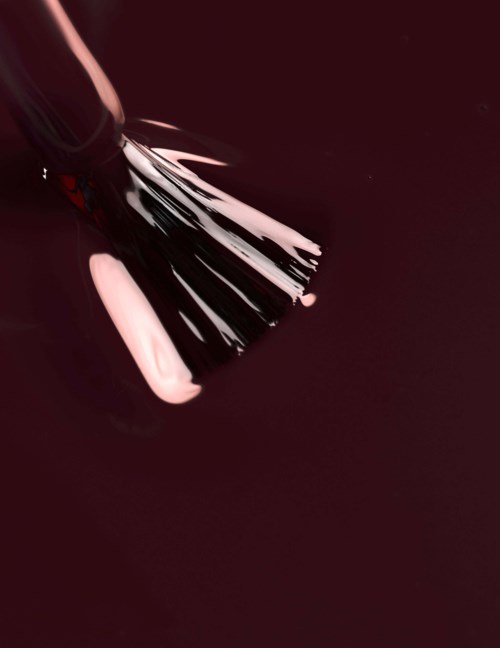 A makeup brush with some pink and white nail polish on a dark red background.