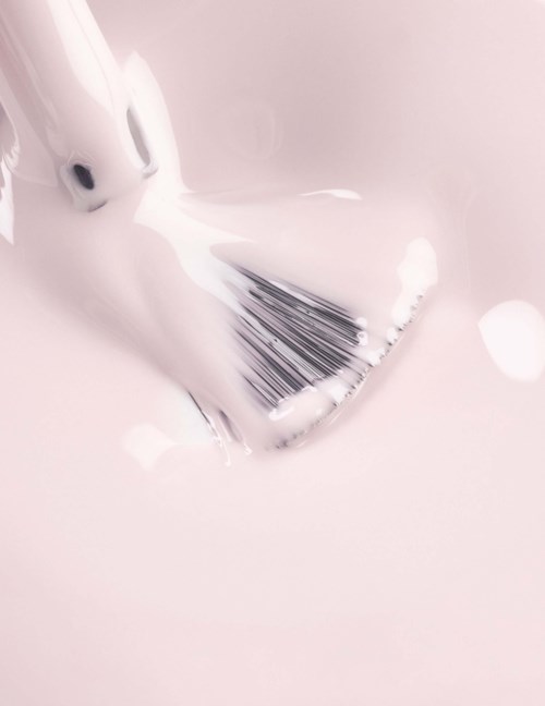 A white makeup brush with black bristles resting on a pink surface, with some powder and soft lights nearby.