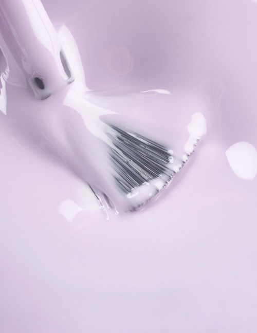 A paintbrush is covered in white paint, with paint spilling around it on a light purple surface.