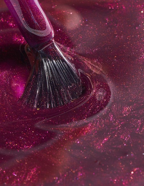 A brush stirs pink, glittery nail polish, creating swirls and sparkles.