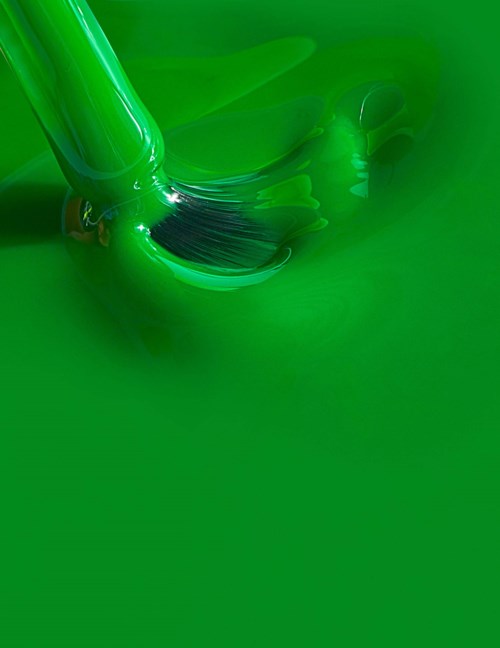 Bright green liquid being poured from a bottle, flowing smoothly and creating a shiny surface.