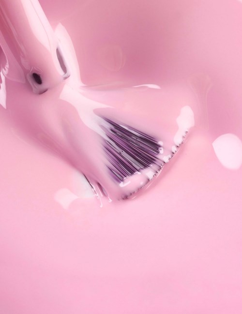 A makeup brush is being cleaned in pink liquid, creating a bubbly foam and splash.